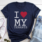 A navy blue t-shirt with the text "I ♥ MY TENANTS" printed on it, along with a red heart symbol. The t-shirt is laid out on a white surface, with a pair of jeans and white sneakers visible in the background.
