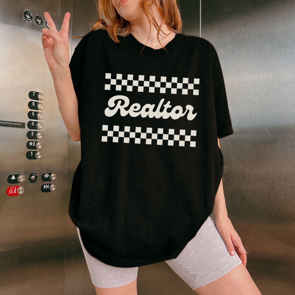 A person wearing a black t-shirt with the word "Realtor" printed on it, standing in front of an elevator.