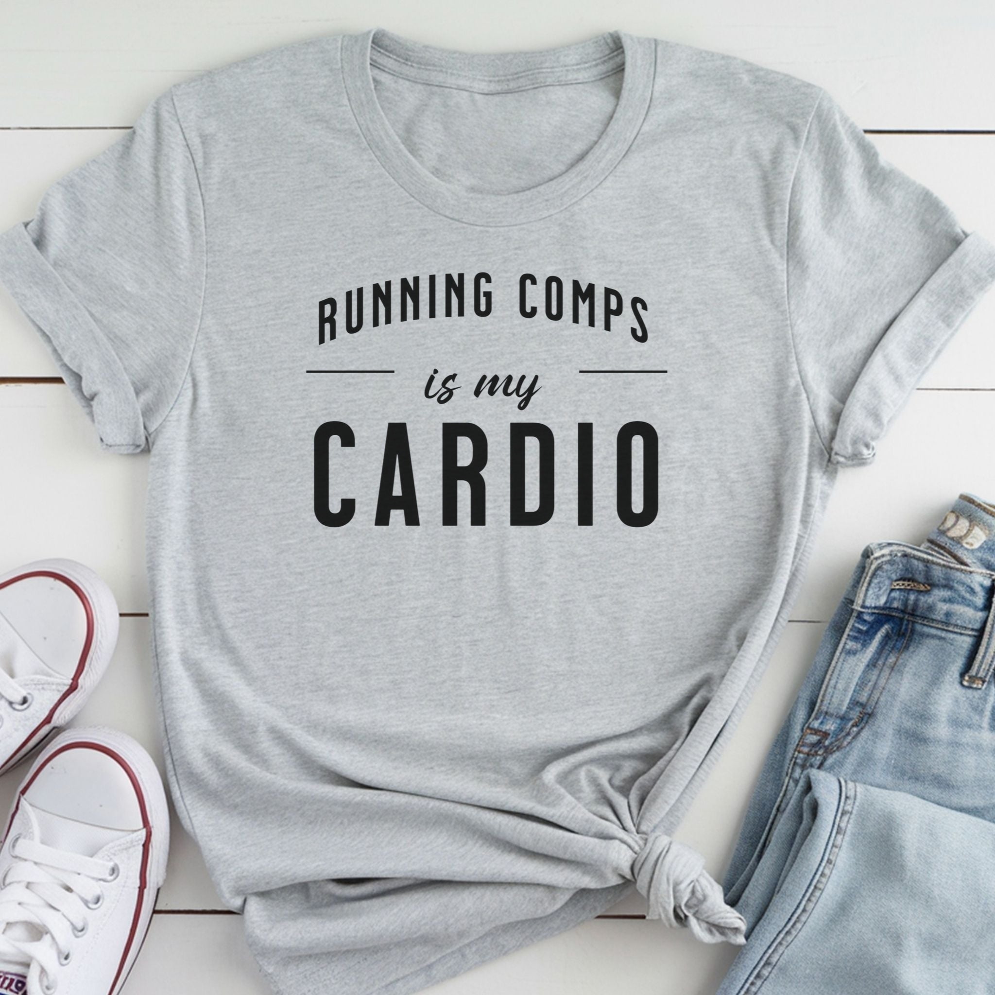 A gray t-shirt with the text "RUNNING COMP'S IS MY CARDIO" printed on it, along with a pair of jeans and white sneakers.