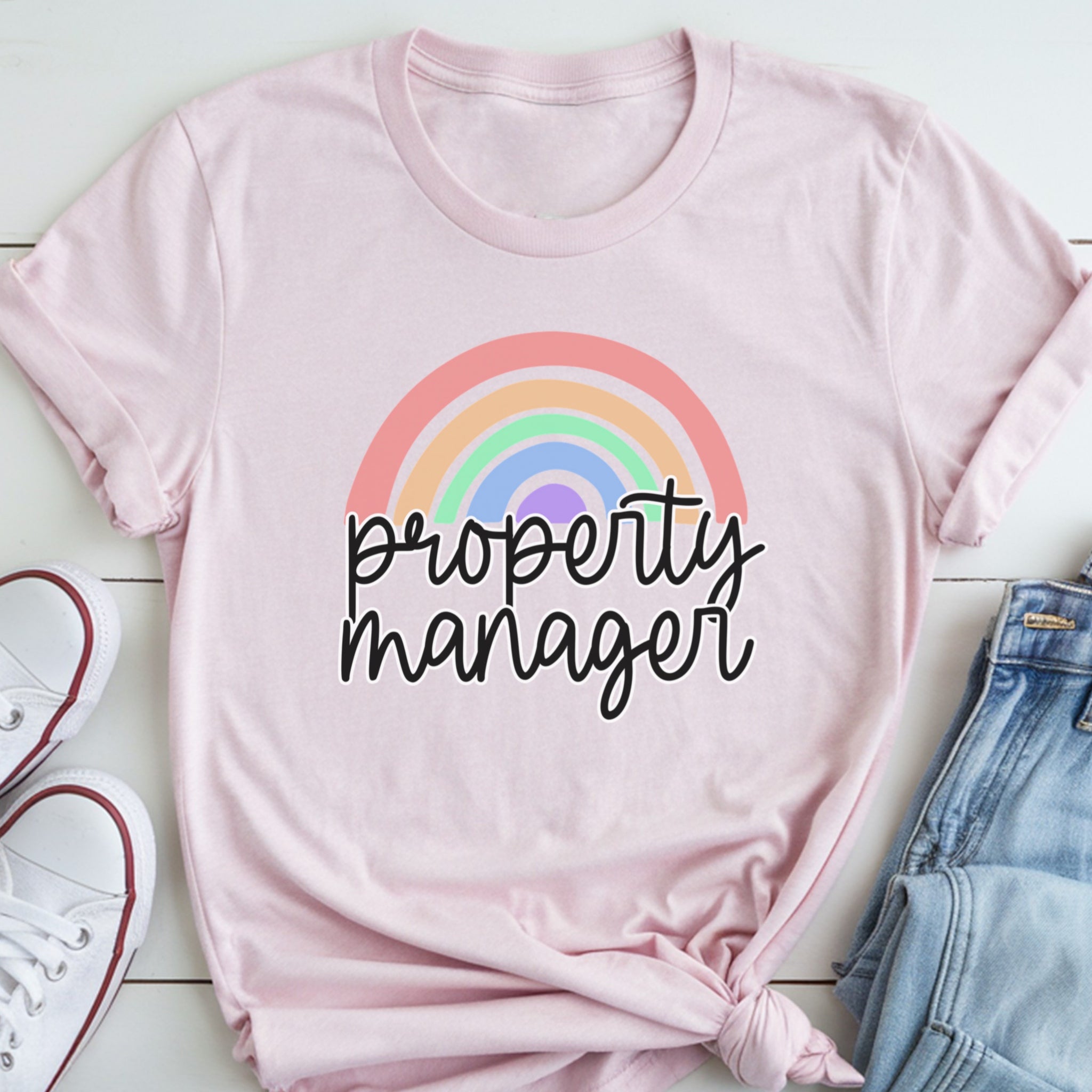 A pink t-shirt with a rainbow graphic and the text "Property Manager" printed on it, along with a pair of jeans and white sneakers.