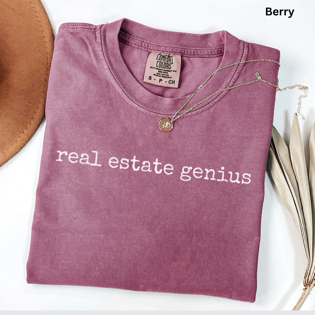 a purple t-shirt with the text "real estate Genius" printed on it, along with a necklace and a hat.