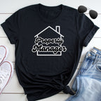 A black t-shirt with the text "Property Manager" printed on it, along with a graphic of a house, is laid out on a white surface next to a pair of jeans and sunglasses.