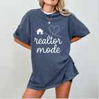 A woman wearing a blue t-shirt with the text "realtor mode" printed on it, along with a small house and heart symbol.