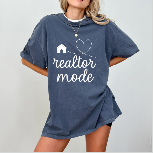 A woman wearing a blue t-shirt with the text "realtor mode" printed on it, along with a small house and heart symbol.