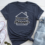 A dark blue t-shirt with the text "Property Manager" printed on it, along with a graphic of a house. The t-shirt is laid out on a wooden surface, accompanied by a pair of jeans and a pair of white sneakers.