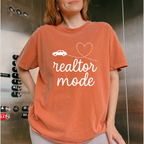 A woman wearing a red t-shirt with the text "realtor mode" printed on it, standing in front of an elevator.