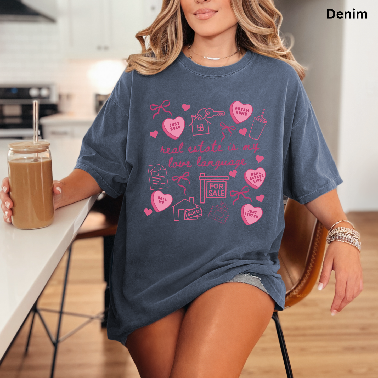 A woman wearing a blue t-shirt with a graphic design printed on it, sitting at a table with a drink in a glass.