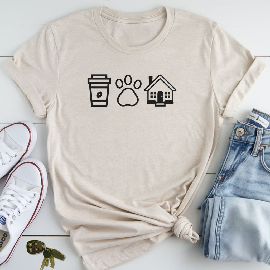 A beige t-shirt with a graphic design of a coffee cup, paw print, and house, along with a pair of jeans and sneakers, all laid out on a white surface.