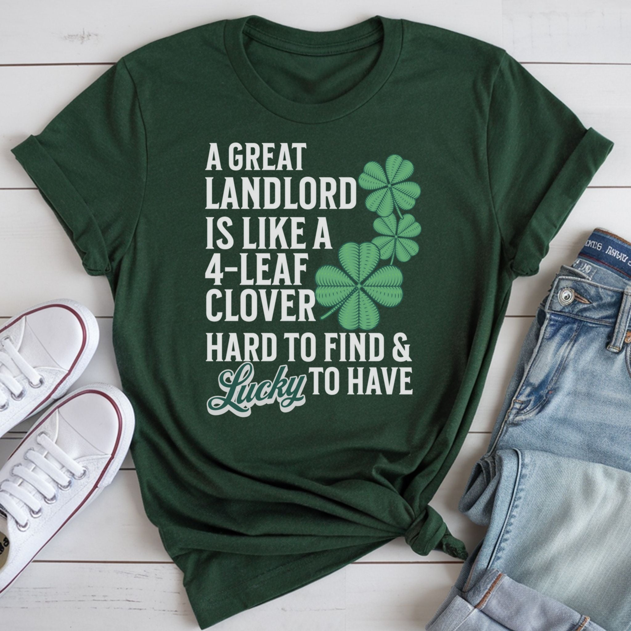 A green t-shirt with white text and clover graphics, along with a pair of jeans and white sneakers, all laid out on a white surface.