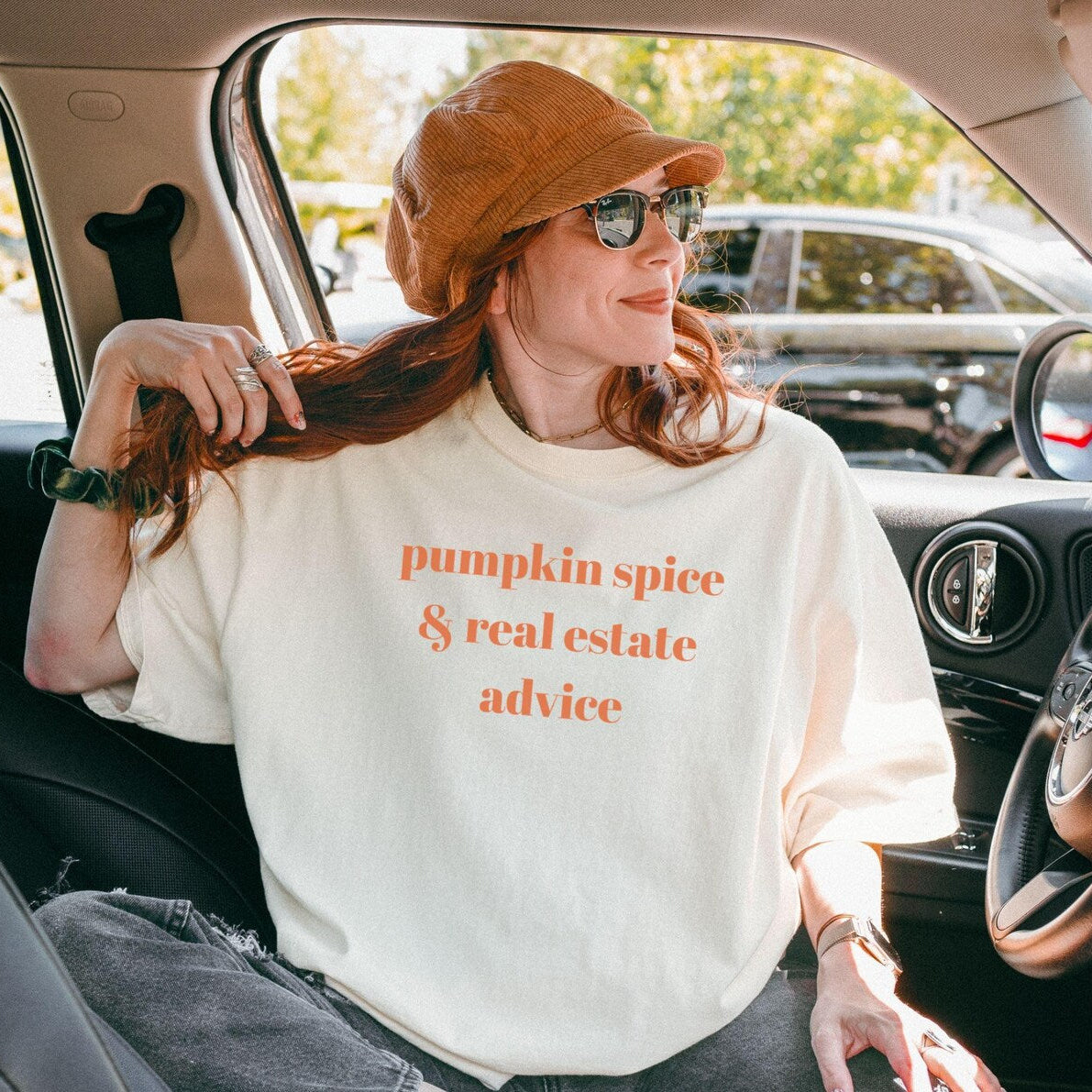 Woman sitting in a car wearing a white sweatshirt with text, sitting in a car.